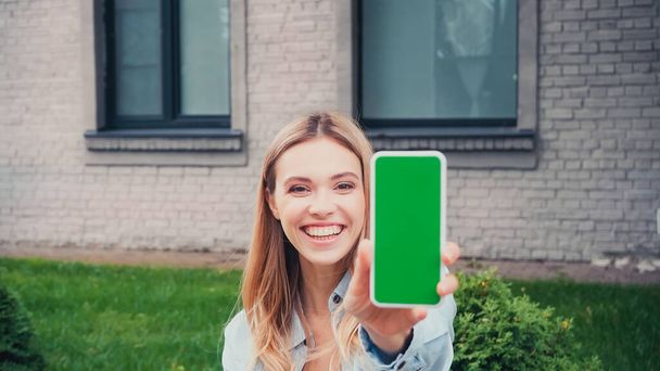 cheerful student holding smartphone with green screen near building  - Photo, Image