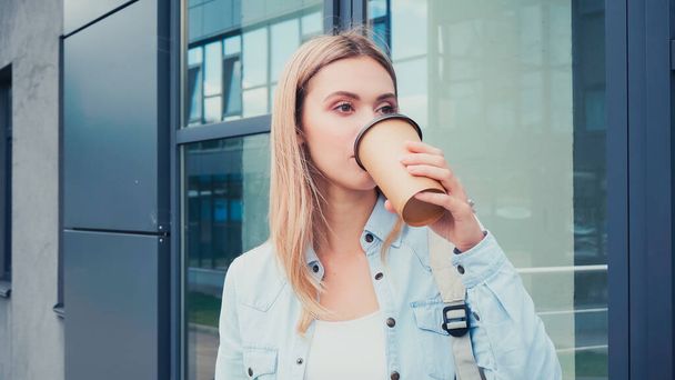 junge Frau trinkt Kaffee, um sich Gebäude in der Stadtstraße zu nähern - Foto, Bild