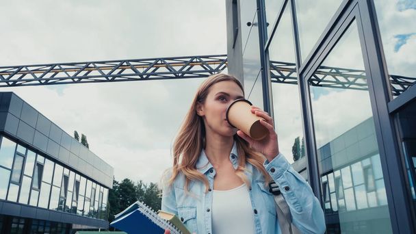 Junge Studentin trinkt Kaffee to go, während sie auf der Straße geht  - Foto, Bild