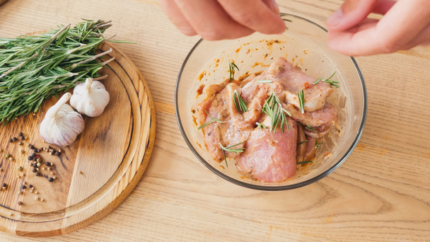 top view of chef seasoning marinated sliced chicken with rosemary in bowl - Photo, Image