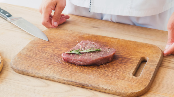 vista parcial del chef de pie cerca de filete de res con rama de romero en la tabla de cortar - Foto, Imagen