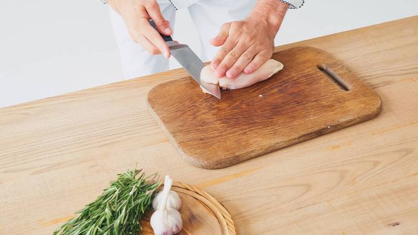 vista parziale dell'uomo che taglia il filetto di pollo vicino agli ingredienti sul tavolo su bianco - Foto, immagini