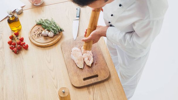 Vista de alto ángulo del chef condimento filete de pollo en la tabla de cortar - Foto, Imagen