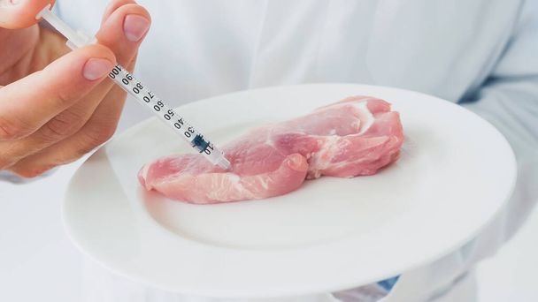 Vista recortada del científico inyectando trozo de carne cruda en el plato - Foto, Imagen