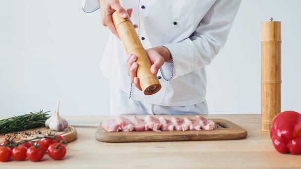 Cropped view of chef with salt mill seasoning pieces of pork tenderloin on white - Fotografie, Obrázek