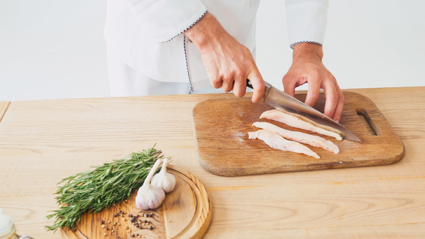 partial view of chef cutting chicken filet on chopping board on white  - Fotoğraf, Görsel