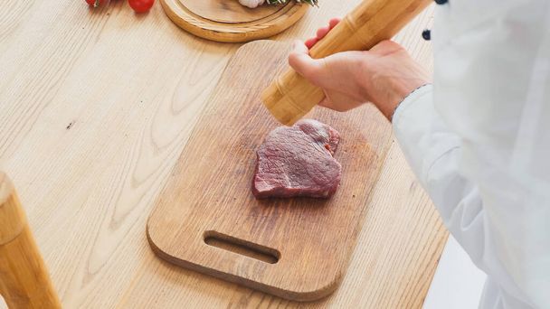 Geoogst uitzicht op chef-kok met molen kruiden rundvlees biefstuk op snijplank - Foto, afbeelding