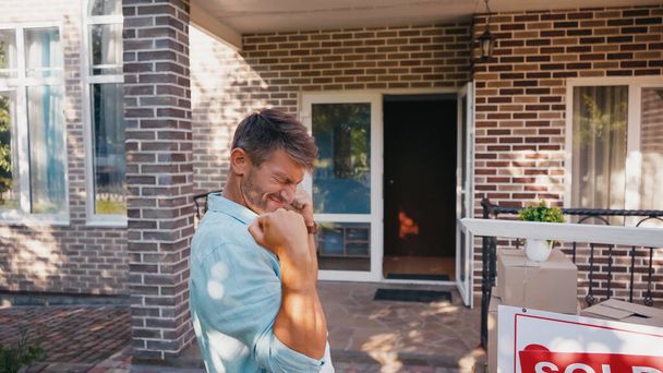 excited man with closed eyes near board with sold lettering and new house  - Photo, Image