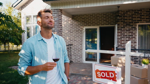 pleased man holding glass of red wine near new house - Photo, Image
