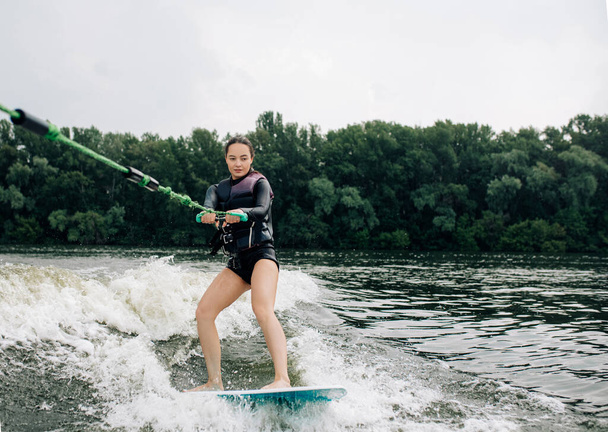 Jeune femme wakesurf sur la rivière est remorqué derrière un bateau à moteur par câble métallique. - Photo, image