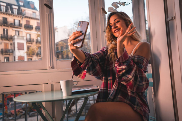 Lifestyle of a young blonde breakfast having breakfast next to the sale of his house. Dressed in underwear and pajamas, greeting in a video call to your boyfriend - Foto, imagen