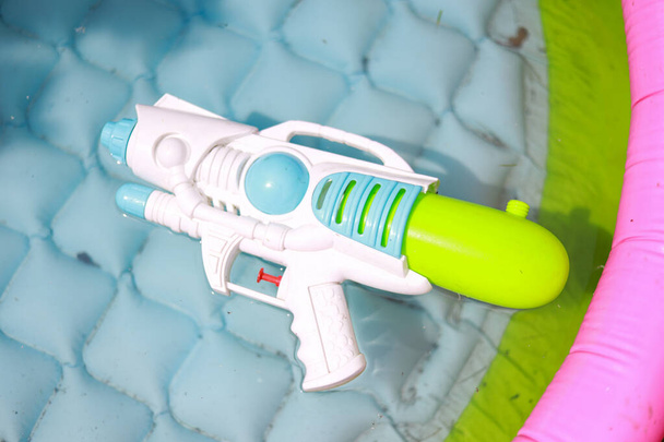 White play watergun laying in small kids toddlers pool filled with water. Photo taken on warm summer day. - Photo, Image