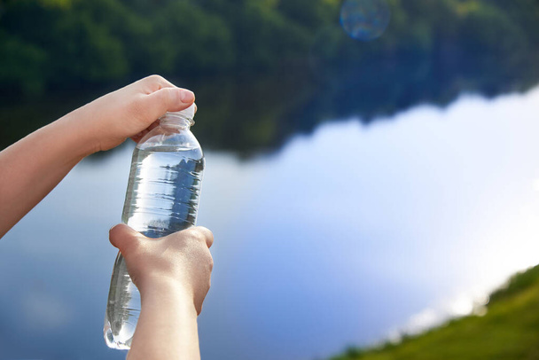 Les mains de la femme tiennent des bouteilles en plastique avec de l'eau potable propre sur le fond de la rivière, concept de mode de vie sain. - Photo, image