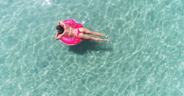 Luchtvaartmaatschappij. Top uitzicht op jong vrij sexy meisje zwemmen met roze zwemmatras aan de oceaan, het dragen van bikini en zonnebril, uitzicht op de oceaan, ontspannen en plezier hebben op vakantie. - Foto, afbeelding