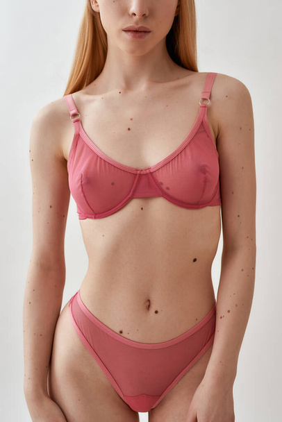 Cropped shot of slim young caucasian woman wearing pink transparent underwear posing isolated over light gray background - Foto, afbeelding