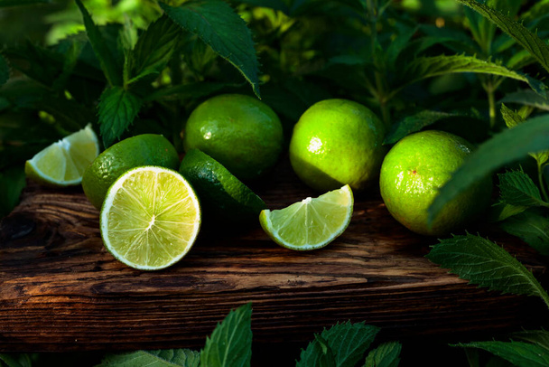 Limes and growing mint in the garden. Lime slices and mint leaves on an old wooden background. - Zdjęcie, obraz