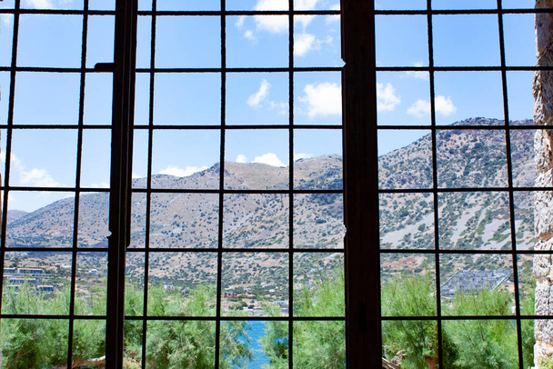 Insel Spinalonga, Blick auf die schöne Welt aus dem vergitterten Fenster der Gefängniszelle, Kreta, Griechenland - Foto, Bild