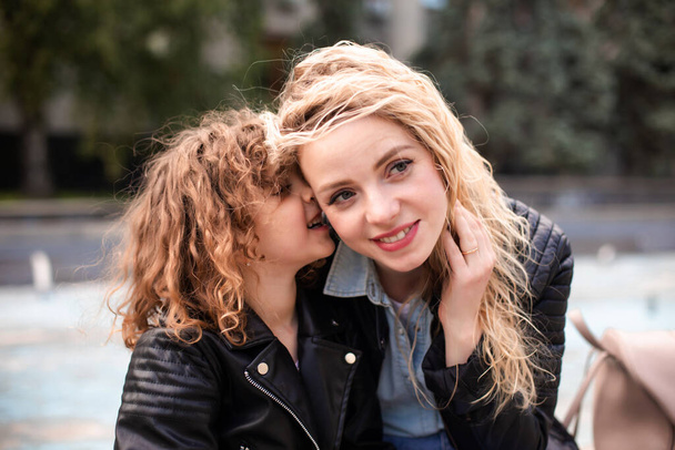 Mom and daughter are whispering while walking around the city - Photo, image