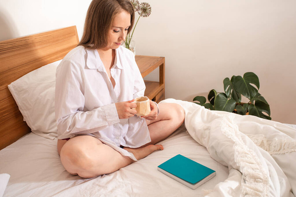 Dreamful girl drinking coffee siting in cosy bed - Valokuva, kuva