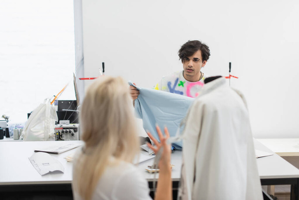 zadní pohled rozmazaného návrháře gestikulujícího při rozhovoru s kolegou se vzorkem tkaniny - Fotografie, Obrázek