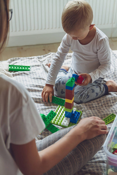 Mom and kid play together in the bedroom on a bed with plastic blocks - Foto, afbeelding