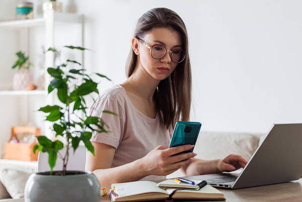 Young woman using mobile phone and laptop to work at home, multiple devices - Φωτογραφία, εικόνα