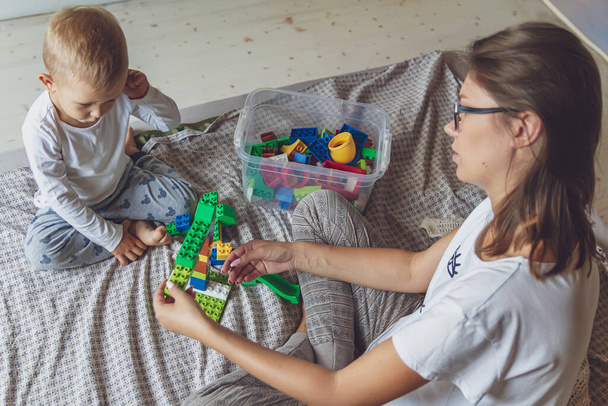 Mom and kid play together in the bedroom on a bed with plastic blocks - Foto, imagen