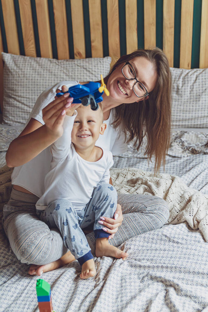 Mom and kid play together in the bedroom on a bed with plastic blocks - Foto, Bild