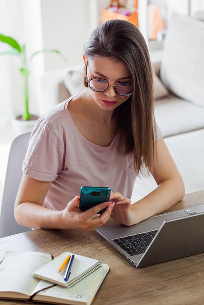 Young woman using mobile phone and laptop to work at home, remote work - Foto, Imagem