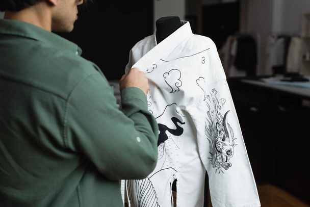 Teilansicht eines verschwommenen Modedesigners in der Nähe von Kimono mit traditioneller Zeichnung auf Schaufensterpuppe - Foto, Bild