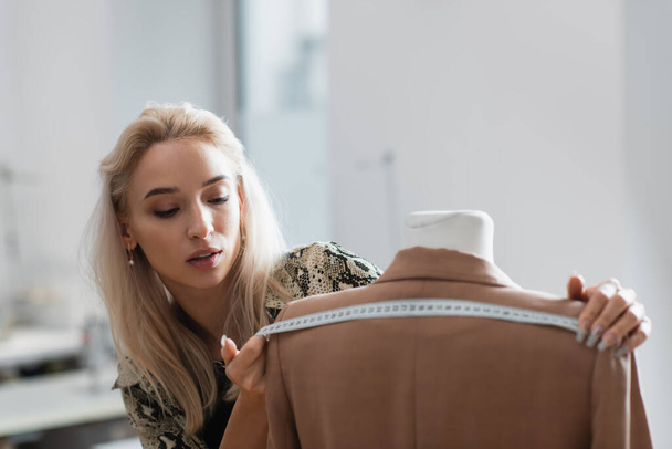 joven diseñador de moda que mide la chaqueta en el maniquí en el taller de moda - Foto, Imagen