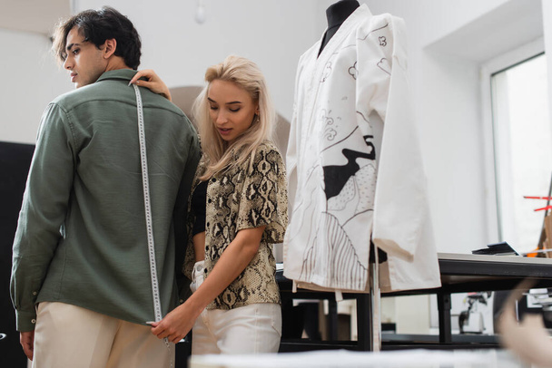 fashionable designer measuring young man in tailor shop - Zdjęcie, obraz