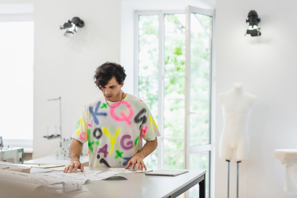 модный модельер смотрит на эскизы и швейные узоры в ателье - Фото, изображение
