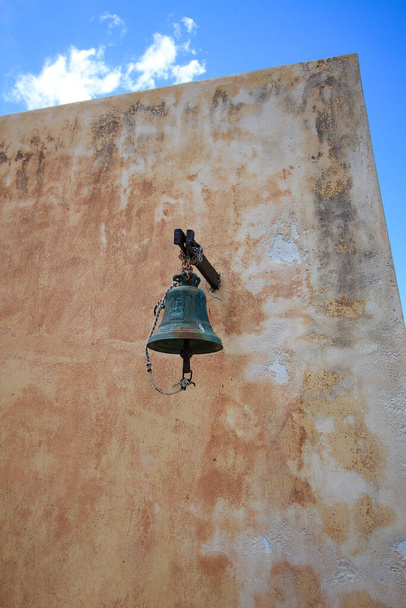An old bell hanging on the wall of an Orthodox church on the island of Spinalonga. - Foto, Imagen