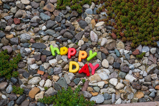 happy day lettering written with toy letters on the stones in the garden of the house - Photo, image