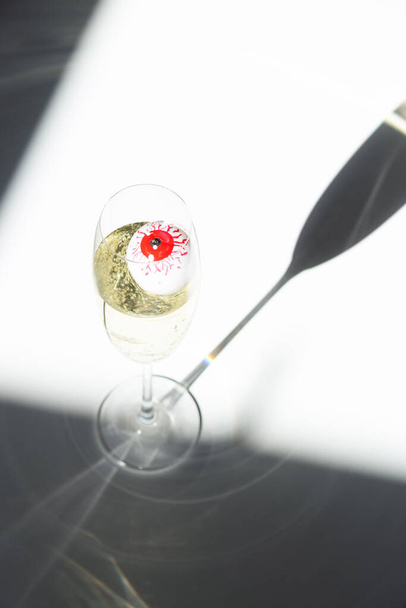 Red eye in a champagne glass in sunlight. Elegant Halloween decor. Autumn holiday concept. Top view, flat lay - Photo, Image