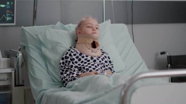 Porträt eines kranken Kinderpatienten, der im Bett liegt und in die Kamera schaut, während er Halswirbelsäule hat - Filmmaterial, Video