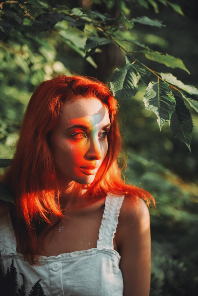 Rainbow face. Rainbow colors reflected on a beautiful redhead girl's face. Forest background - Фото, зображення