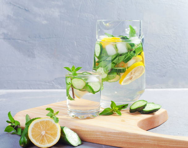 Gezondheidszorg, fitness, gezond voedsel concept. Verse koele munt citroen komkommer giet water, cocktail, detox drank, limonade in een glazen kan. - Foto, afbeelding