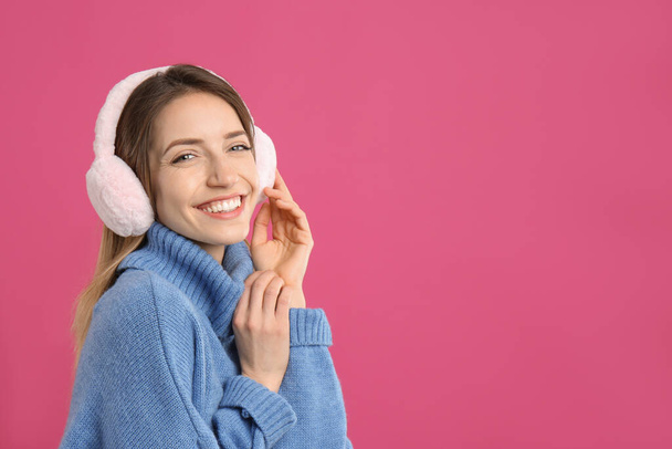 Happy woman wearing warm earmuffs on pink background, space for text - Фото, зображення