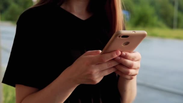 Female hand touching smartphone, scrolling feed on a street. Young woman in shirt using device. Urban style and street fashion. Girl looking down texting on smartphone. Chatting, messaging, reading. - Footage, Video