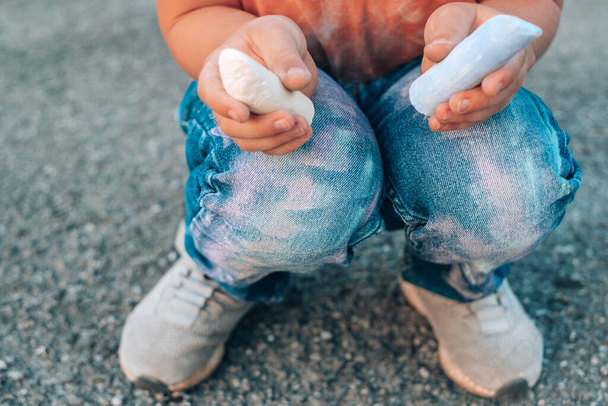 Закрыть грязные пятна мелом на детских штанишках. Мальчик приседает на тротуаре и держит цветной мел в обеих руках. Концепция очистки пятен на одежде. Высокое качество фото - Фото, изображение
