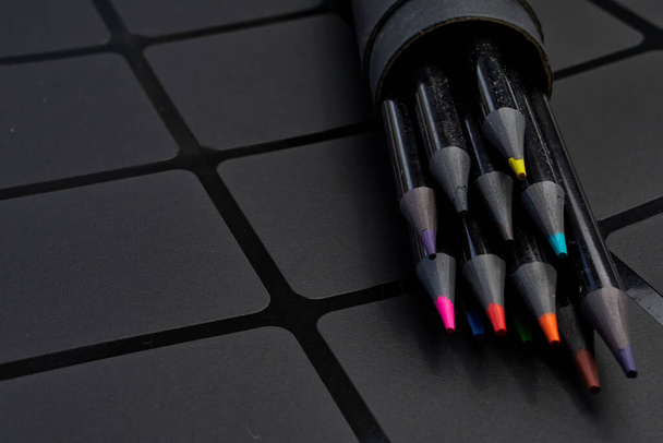 Set van gekleurde potloden in een rond kartonnen kistje op een donkere achtergrond - Foto, afbeelding
