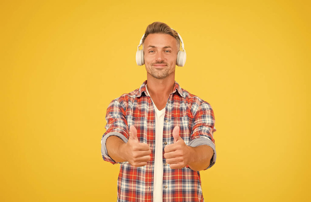 Good music is just a pair of headphones away. Happy man show thumbs ups listening to music yellow background. New technology. Modern life. Fun and entertainment. Loud and clear - Zdjęcie, obraz