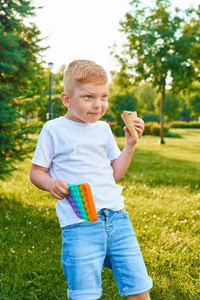 かわいい赤毛の男の子はそれをポップバブル柔軟なフィジェット感覚抗ストレスおもちゃを持っているか、単純なディンプルとアイスクリーム. - 写真・画像