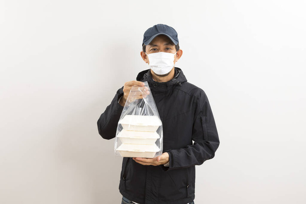 白い背景の上に食品箱を保持保護マスクのアジアの配達人。コロナウイルスの概念  - 写真・画像