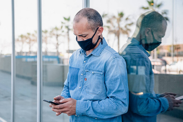 Hombre latino de mediana edad con máscara consulta el teléfono inteligente - Foto, Imagen