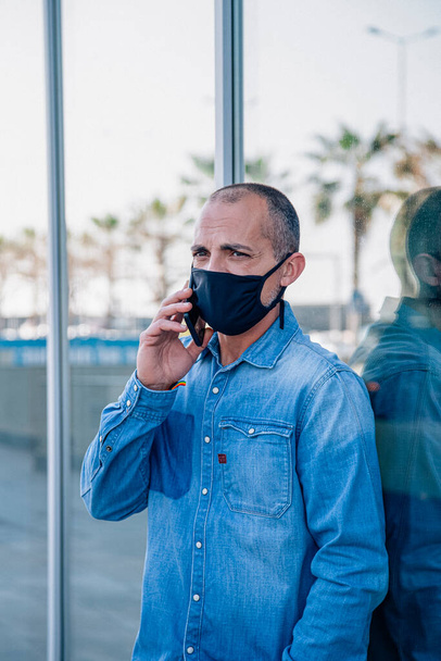 Latino mittleren Alters telefoniert fröhlich mit Gesichtsmaske - Foto, Bild