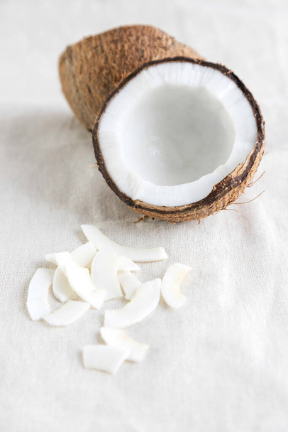 Kokoschips op een linnen tafelkleed en de helft van een verse kokosnoot in de buurt. Een gezonde snack ideaal voor voedingsdeskundigen, veganisten en vegetariërs. - Foto, afbeelding