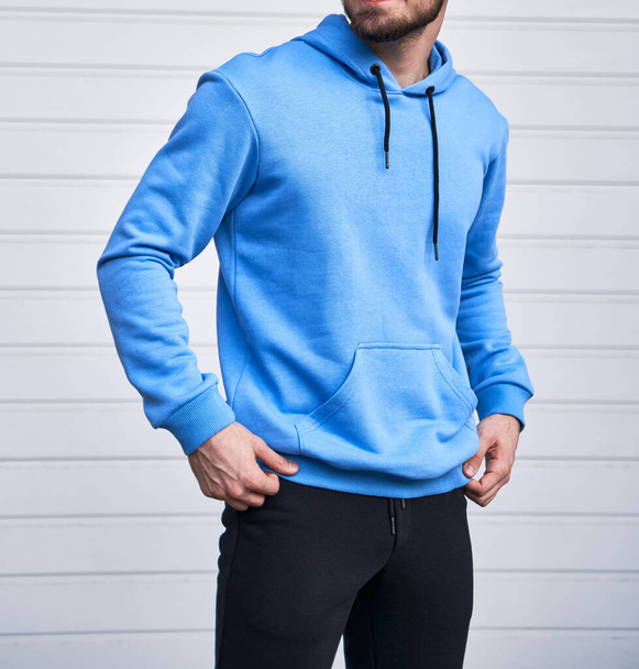 Een man met een baard draagt een blauwe hoodie. Geen logo kleur hoodie. kledinglijn mock up - Foto, afbeelding